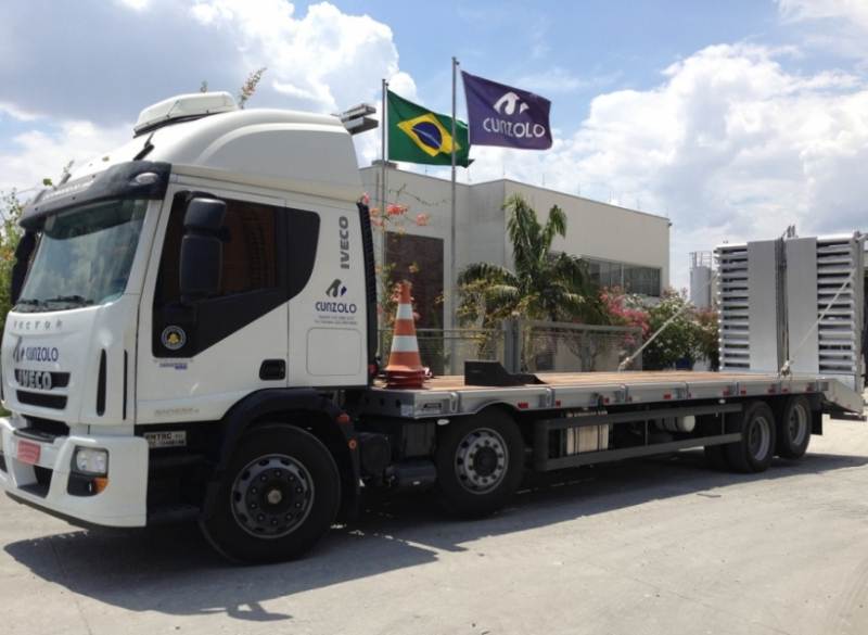 Caminhão Plataforma Carrega Tudo - Transporte Pesado e Remoções Industriais Este caminhão para transporte de cargas pesadas tem uma capacidade útil de 8,90 metros de comprimento e carrega um máximo de 15 toneladas, além de possuir rampa de acesso traseiro em aço com acionamento hidráulico.